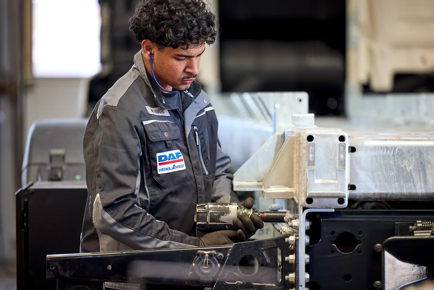 Ein Mechaniker in Arbeitskleidung und Handschuhen arbeitet mit einem Elektrowerkzeug an einem Metallrahmen.