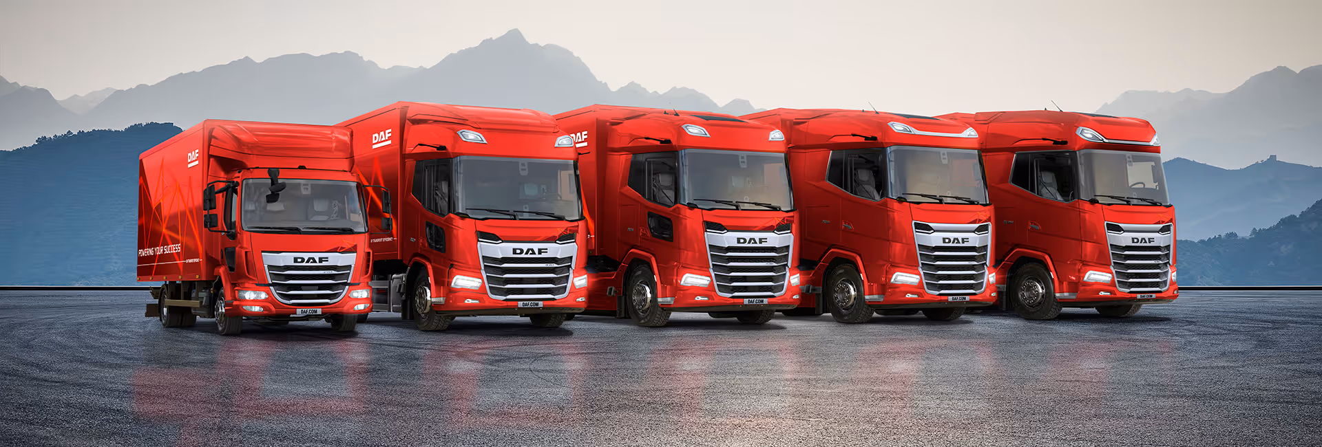 Fünf rote DAF-LKWs der neuen Generation stehen nebeneinander auf einem Asphaltplatz mit Bergkulisse im Hintergrund.