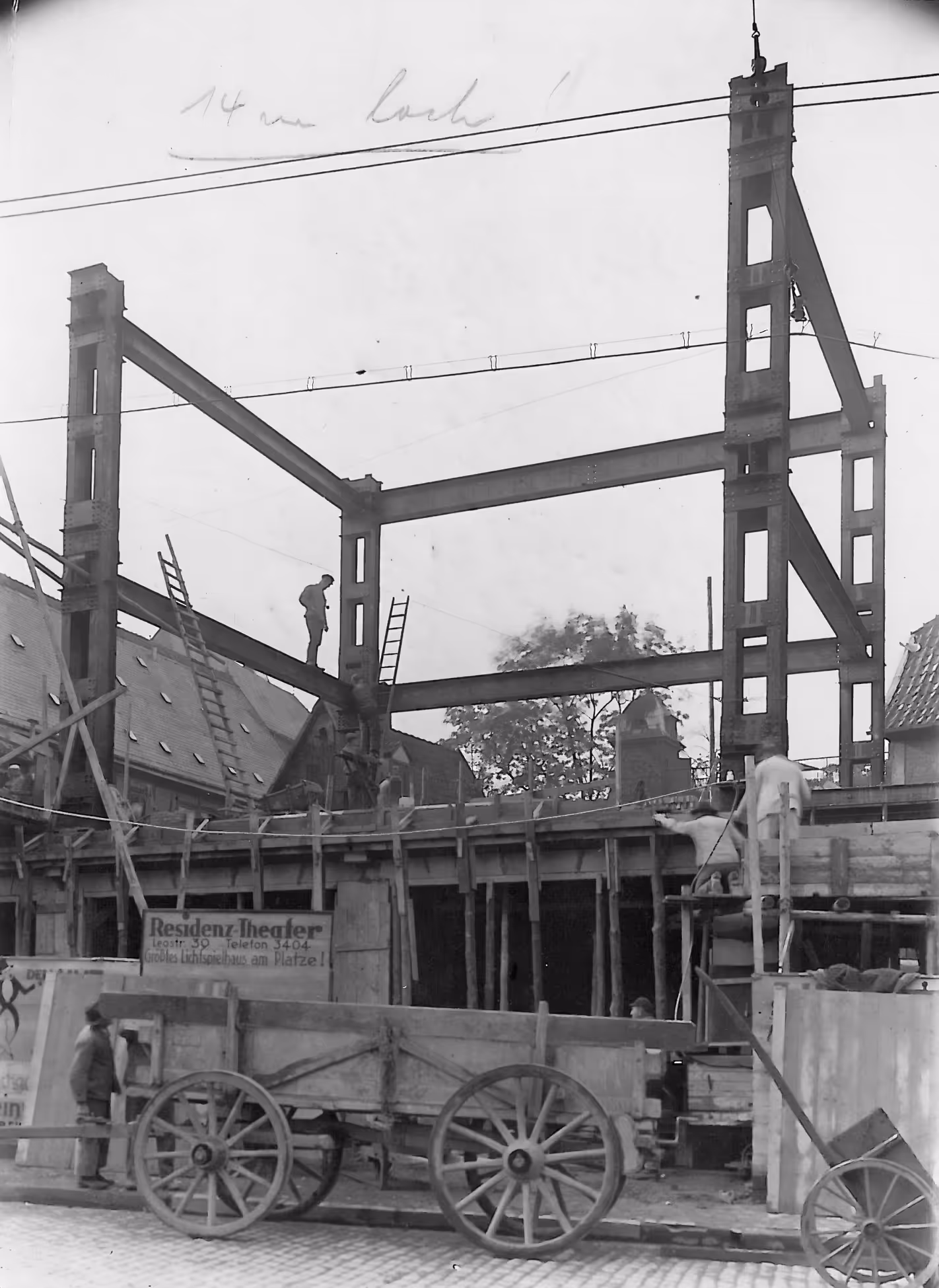 Schwarz-weiß-Foto vom Bau des Residenz-Theater in Paderborn mit einem Gerüst aus Stahlträgern, Bauarbeitern und einem Holz-Wagen vor einem historischen Gebäude.