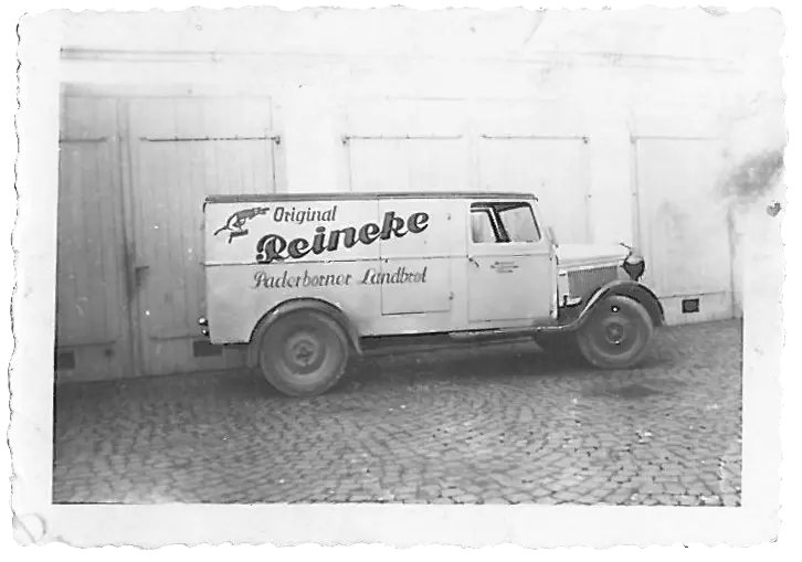 Schwarz-weiß-Foto eines historischen Lieferwagens mit der Aufschrift ‚Original Reineke Paderborner Landbrot‘ auf Kopfsteinpflaster vor einer Gebäudewand.