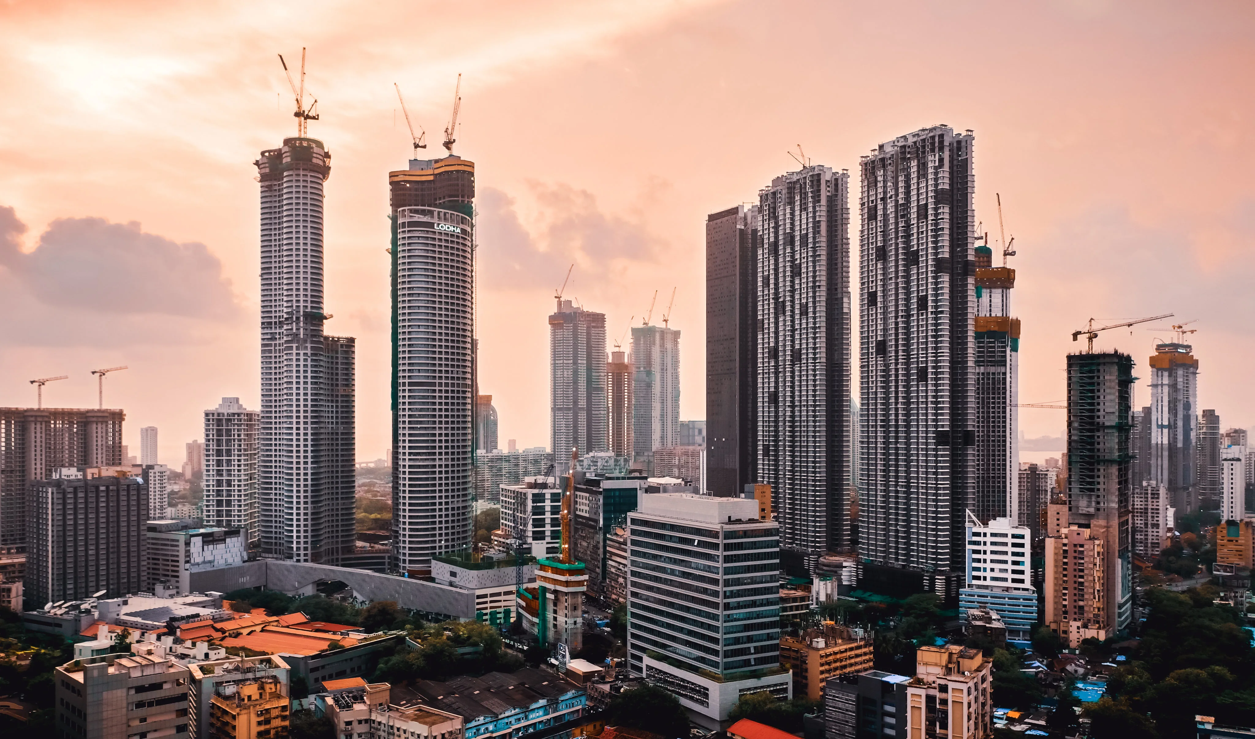 Tall skyscrapers under construction in a city at sunset, with cranes on top of the buildings.