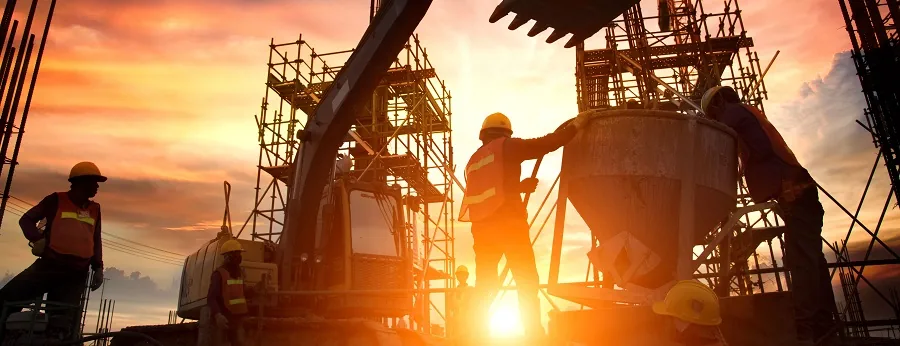 Construction workers in safety vests and helmets working at a building site during sunset, with scaffolding and machinery in the background.