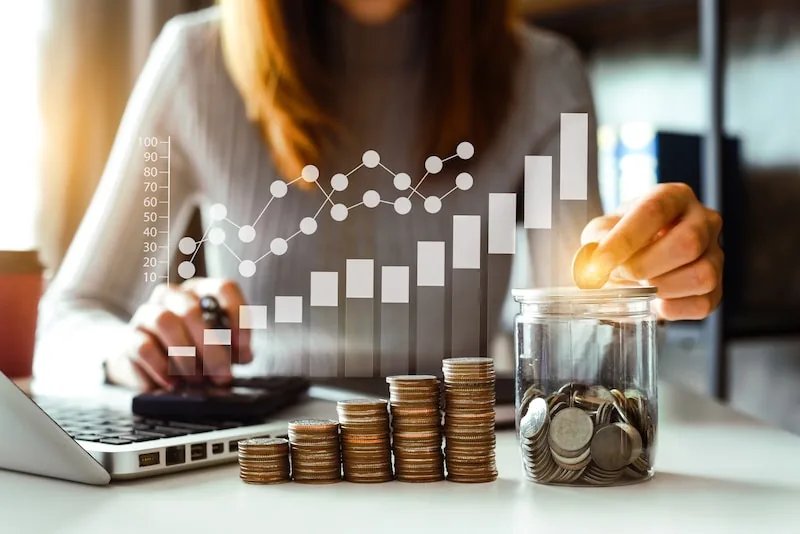 A woman in front of laptop,calculator and coins with an overlay of chart .