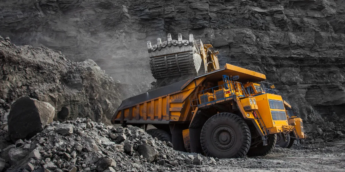 A large yellow mining dump truck being loaded with rocks by an excavator.
