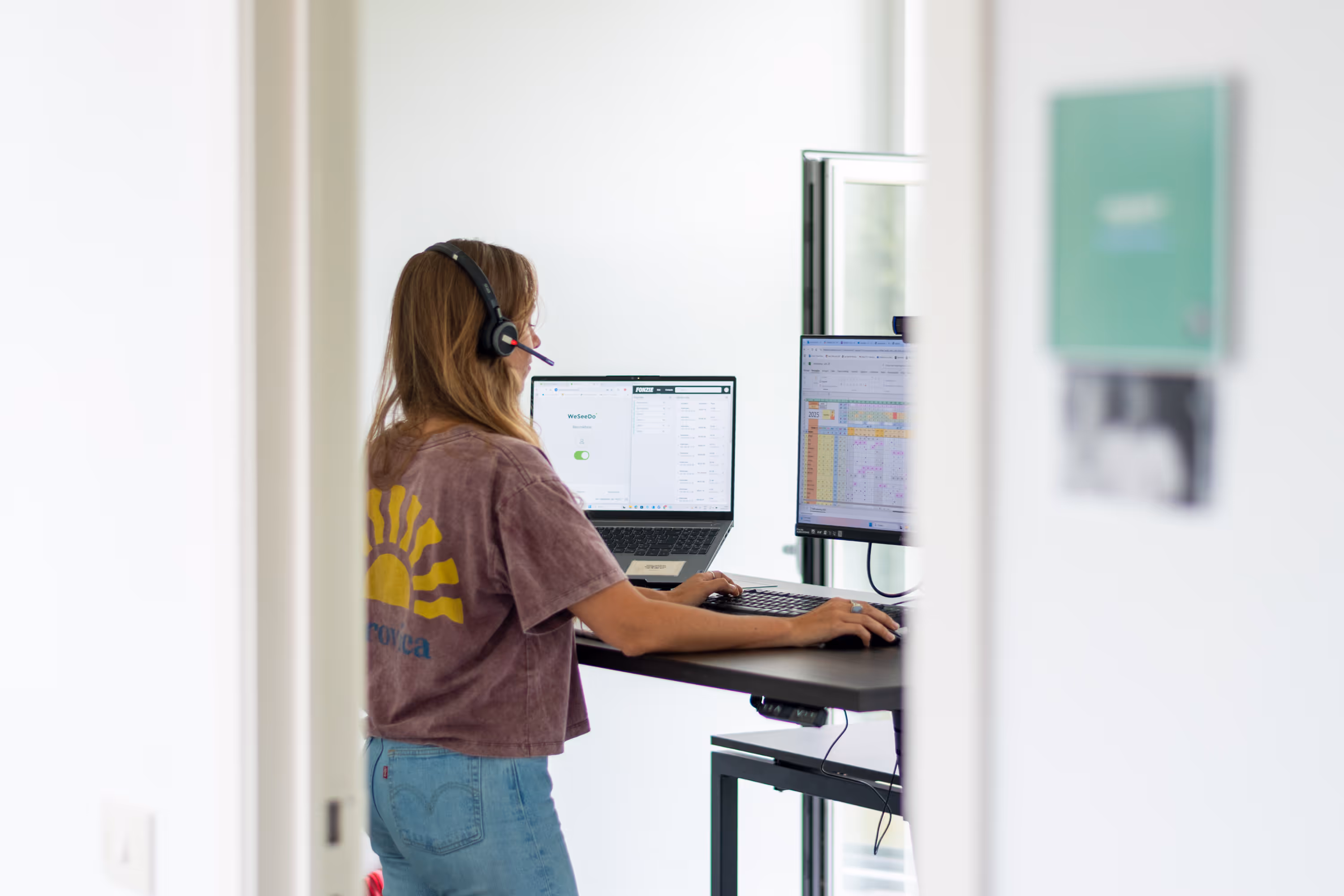 Een vrouwelijke begeleider met headset aan het werk aan een stabureau.