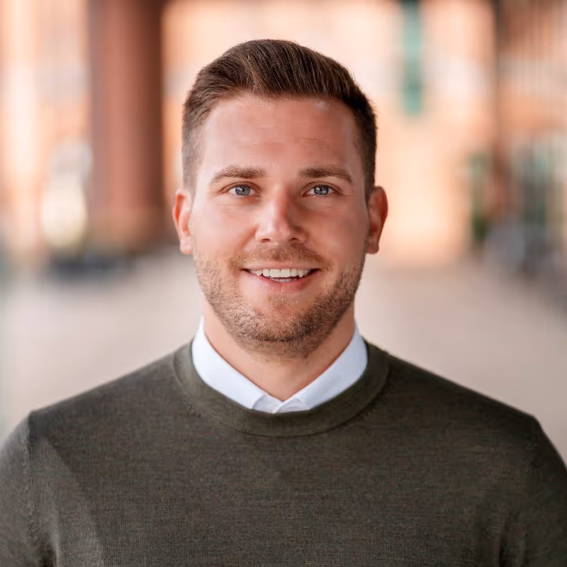 A man with a green sweater and white shirt smiling.
