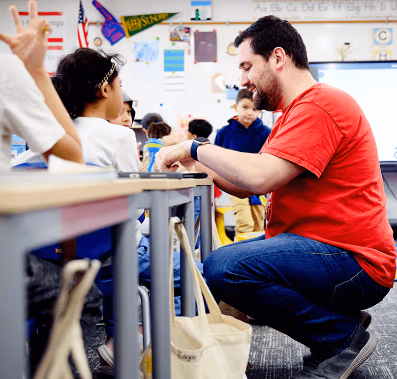 teacher crouching down and helping student at desk