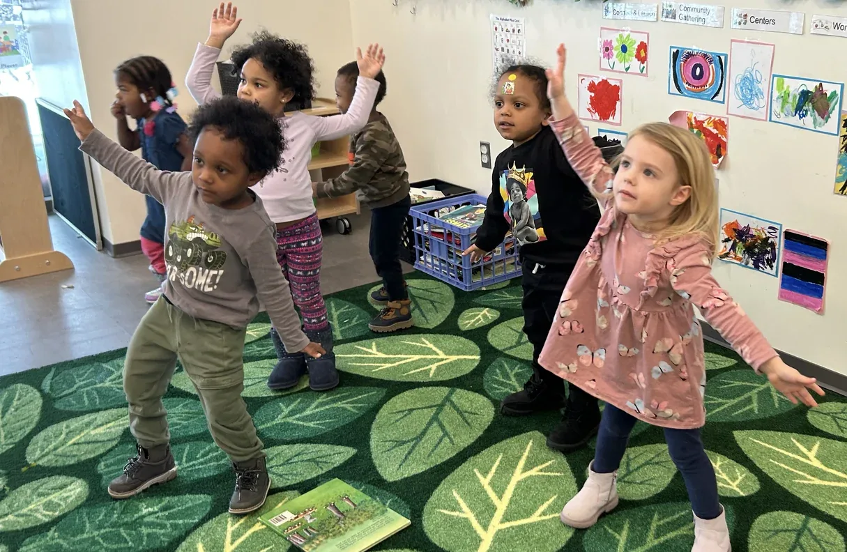 Pre-K children doing a movement activity together on a leaf-patterned rug