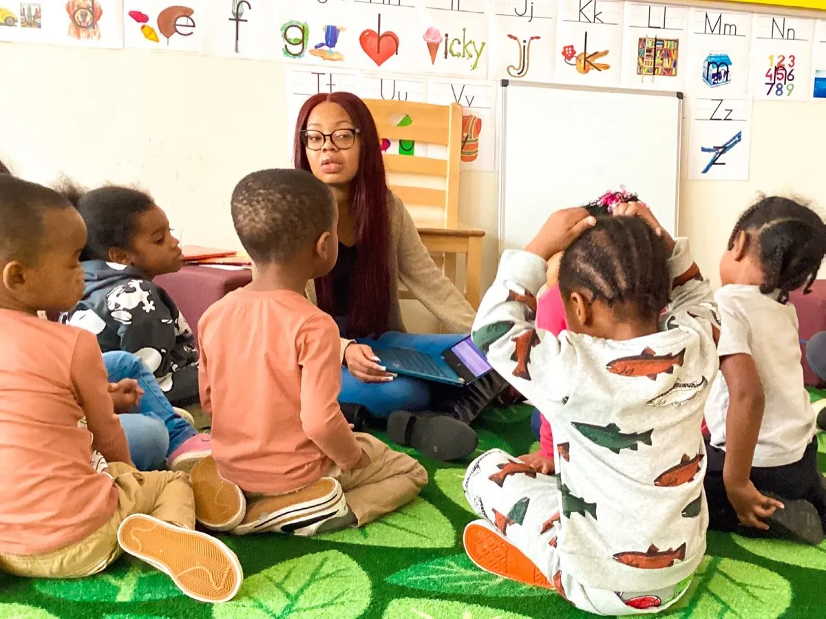 A teacher reading with a group of pre-K children seated on a rug