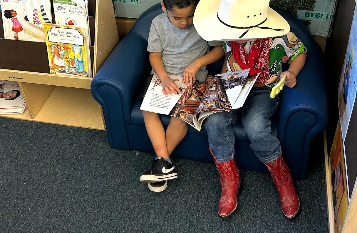 Two children reading together on a blue child-size couch, one in a cowboy hat