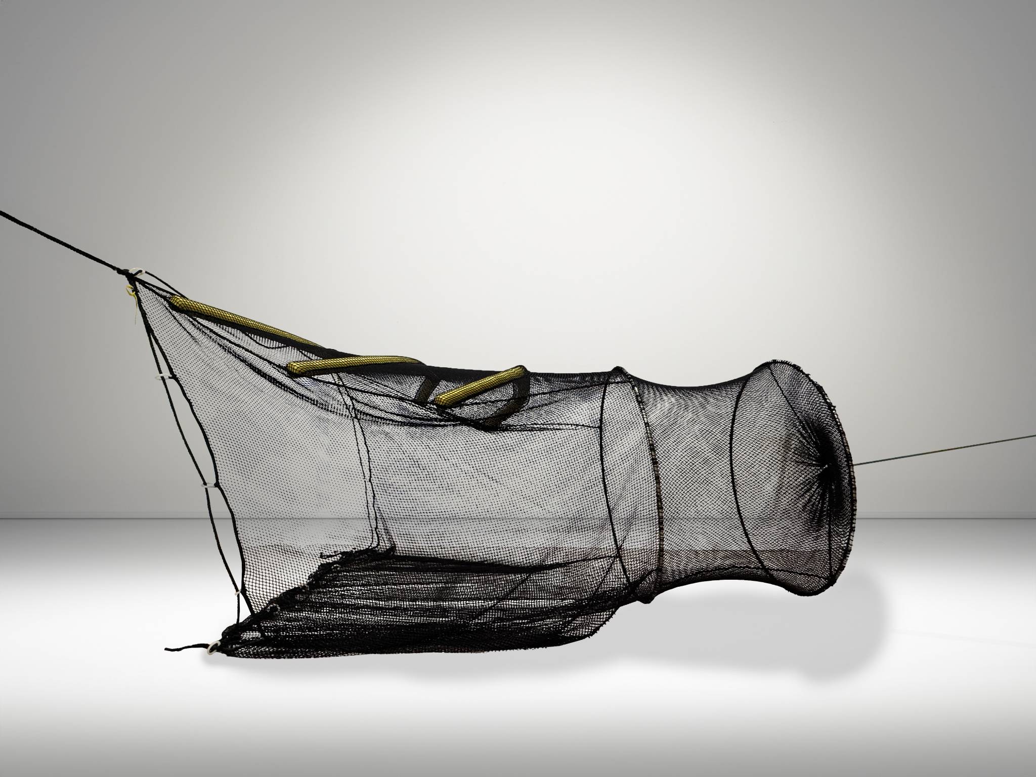 Side view of a black fishing trap made of netting with yellow float elements.