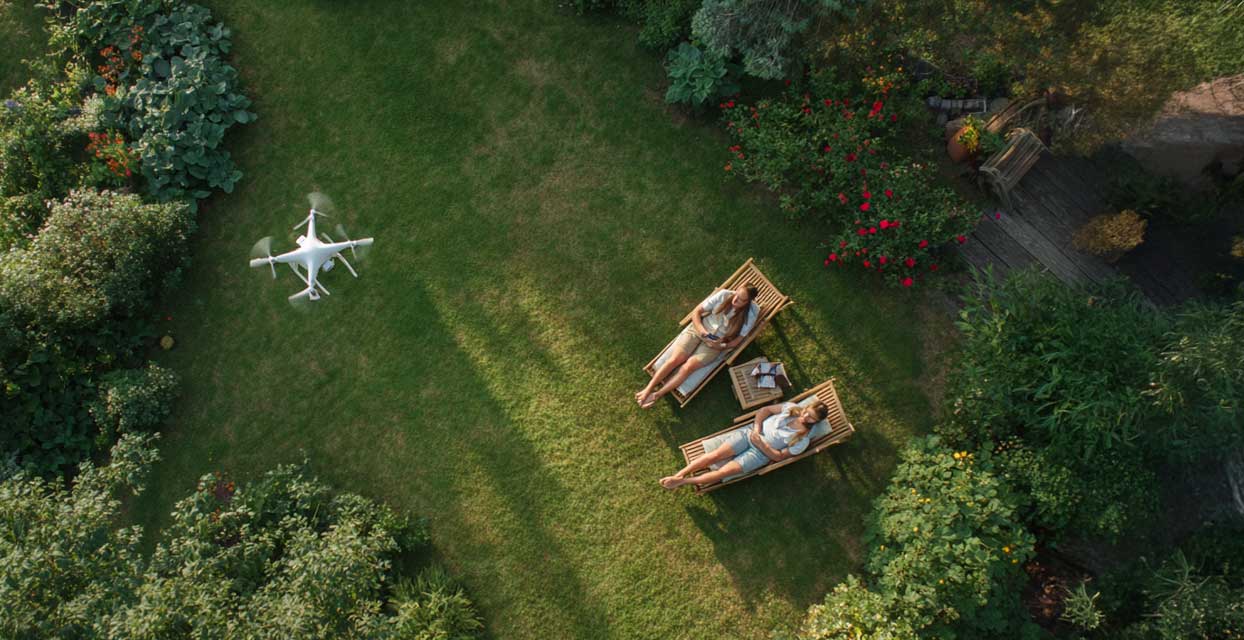 Drohne fliegt über privaten Garten. Zwei Menschen im Gartenstuhl
