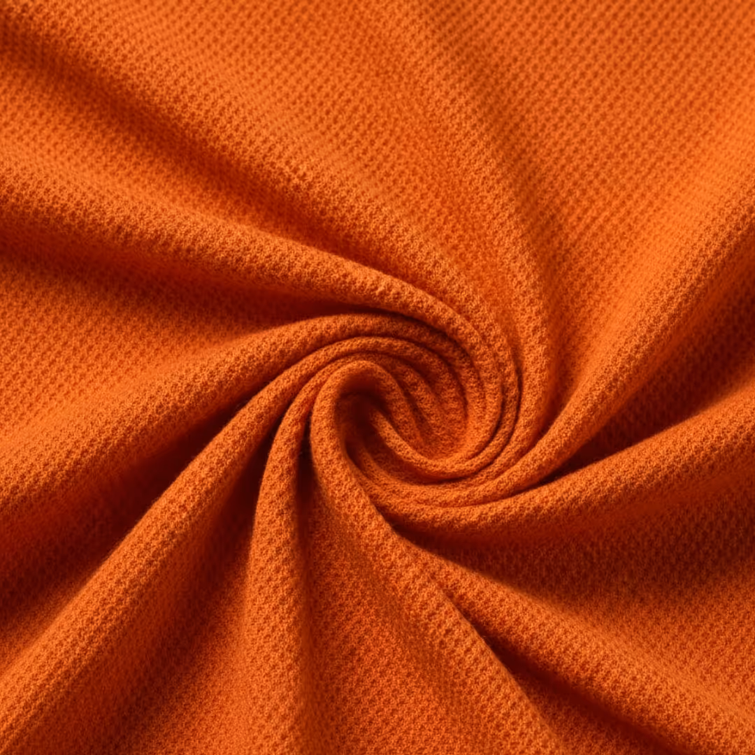 Close-up of orange textured piqué fabric twisted in a swirl pattern.