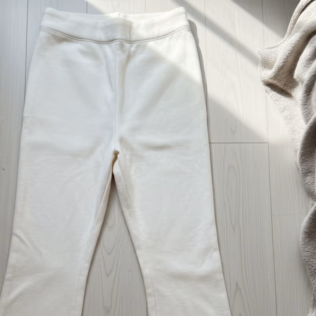Pair of white sweatpants laid flat on a light wood floor next to a beige textured fabric.
