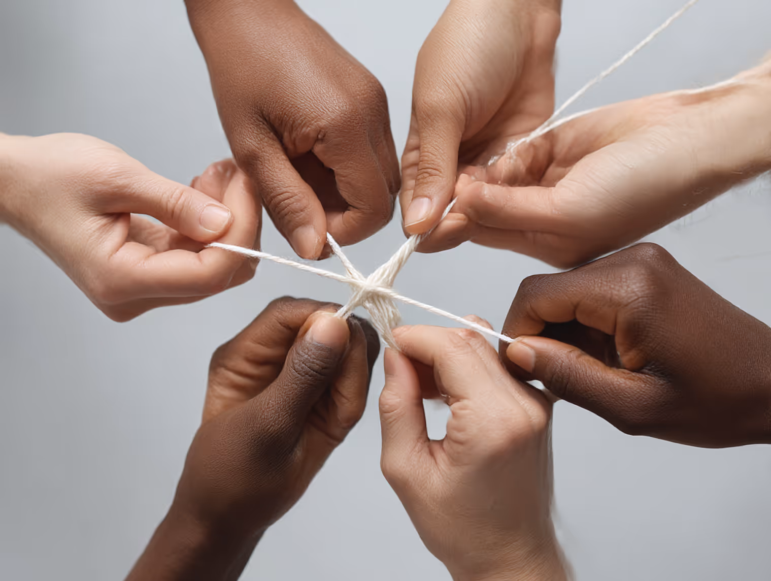 Diverse hands working together to intertwine white string in a star shape.