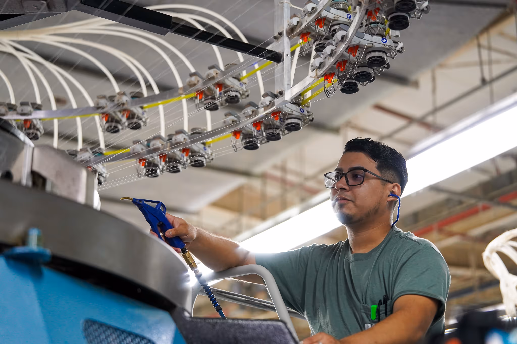 Man wearing glasses and ear protection operating industrial textile machinery.