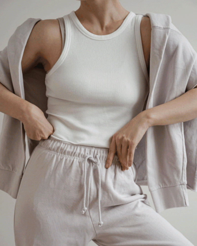 Person wearing a white ribbed tank top with light beige sweatpants and a matching light beige hoodie draped over shoulders.