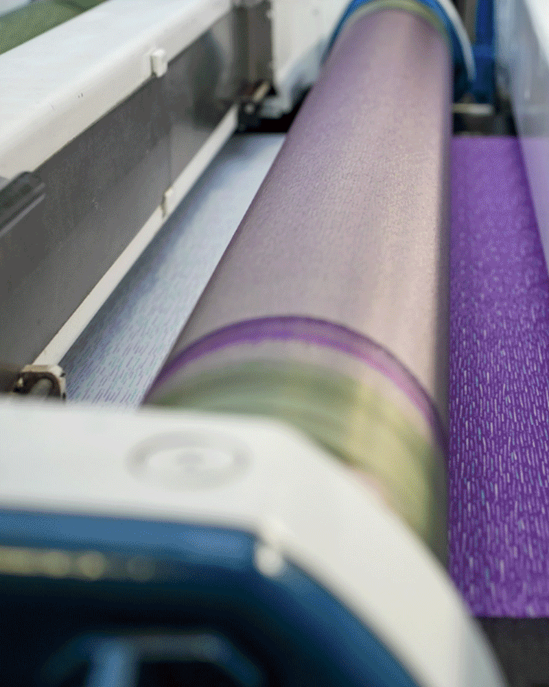 Close-up view of a textile printing machine applying a purple pattern on fabric.