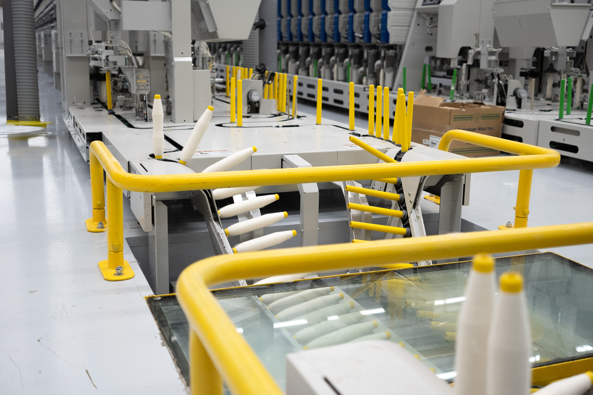 Industrial textile manufacturing machine with yellow safety rails and white yarn cones.
