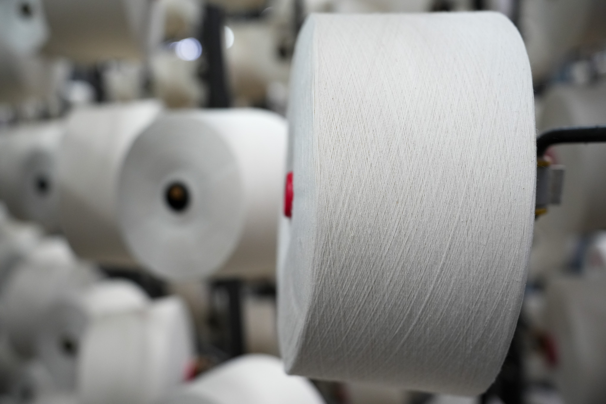 Large spools of white textile yarn on industrial equipment in a factory.