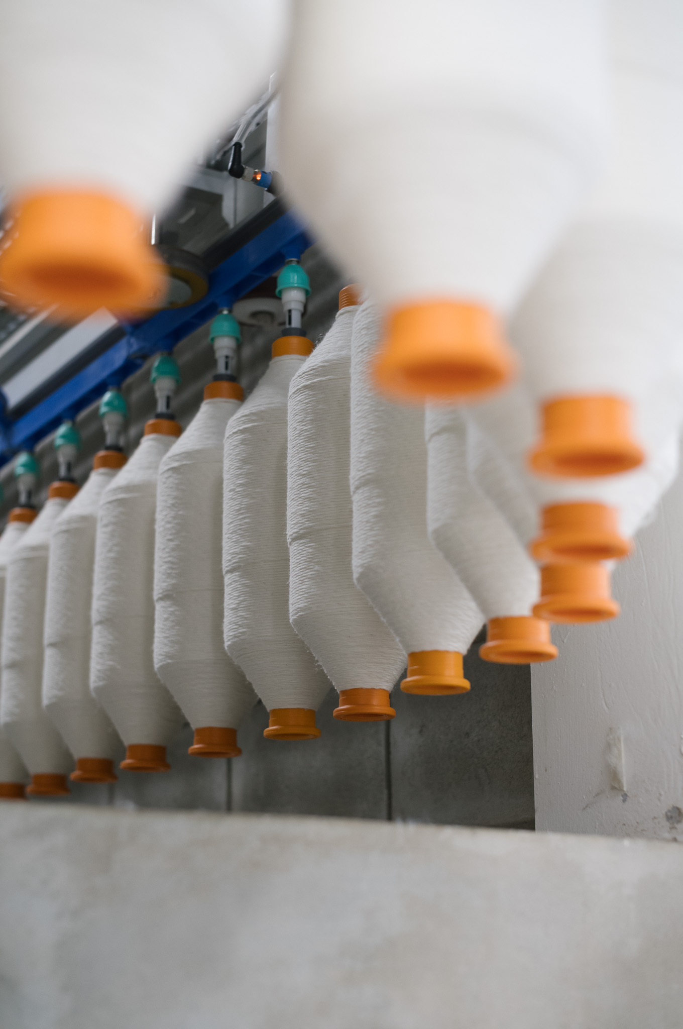 Rows of white yarn spools with orange ends hanging from a textile machine.