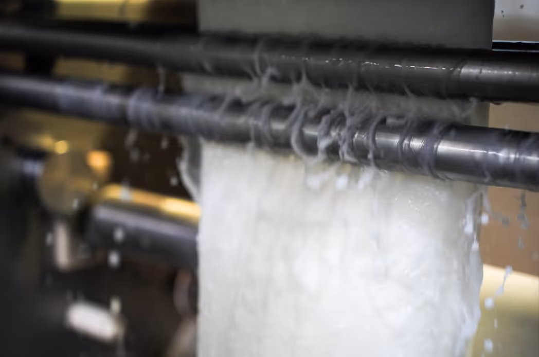 Machine cutting or processing a sheet of white material with spiral shavings falling off.