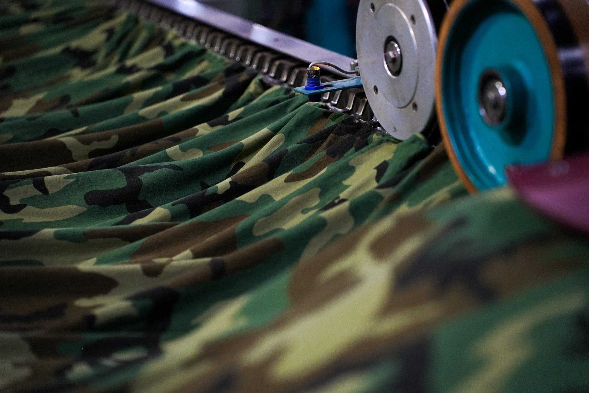Close-up of camouflage fabric being processed through an industrial pleating machine.