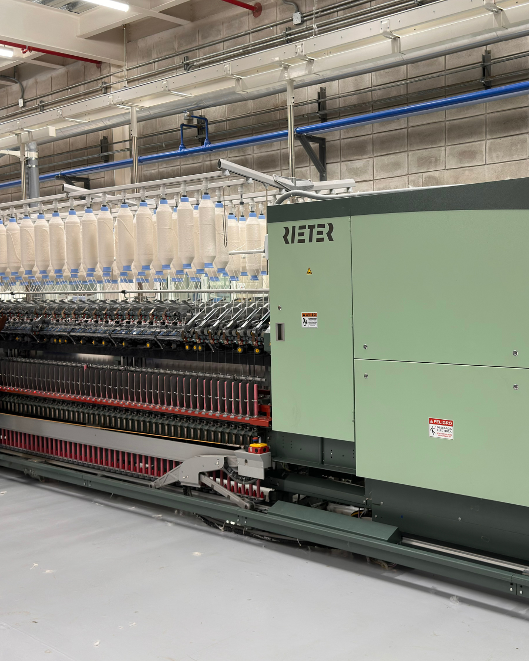 Industrial textile machine with multiple spools of white thread in a factory setting.