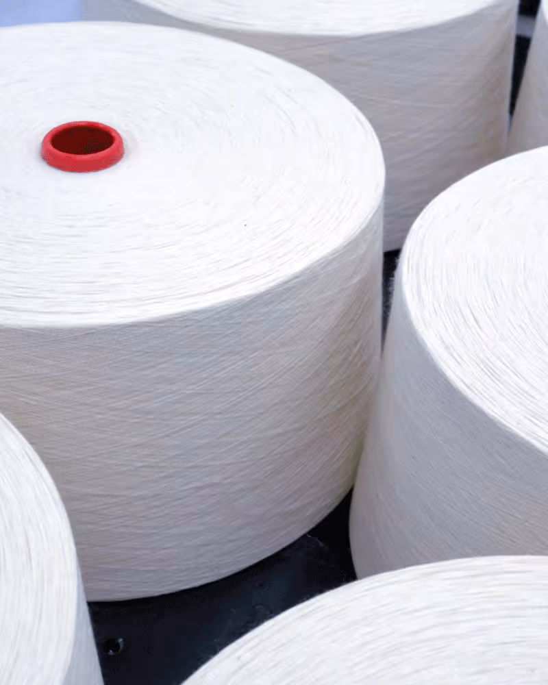 Large industrial spools of white yarn with a red center core.