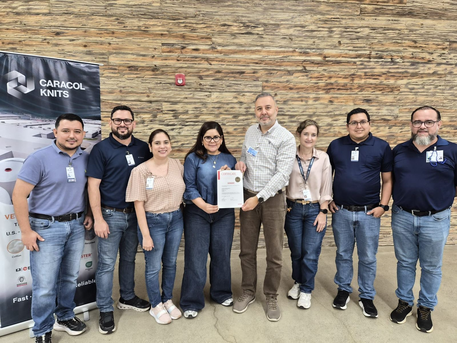 Man wearing glasses and a white shirt with Caracol Knits logo operating textile machinery with yarn threads in an industrial setting.