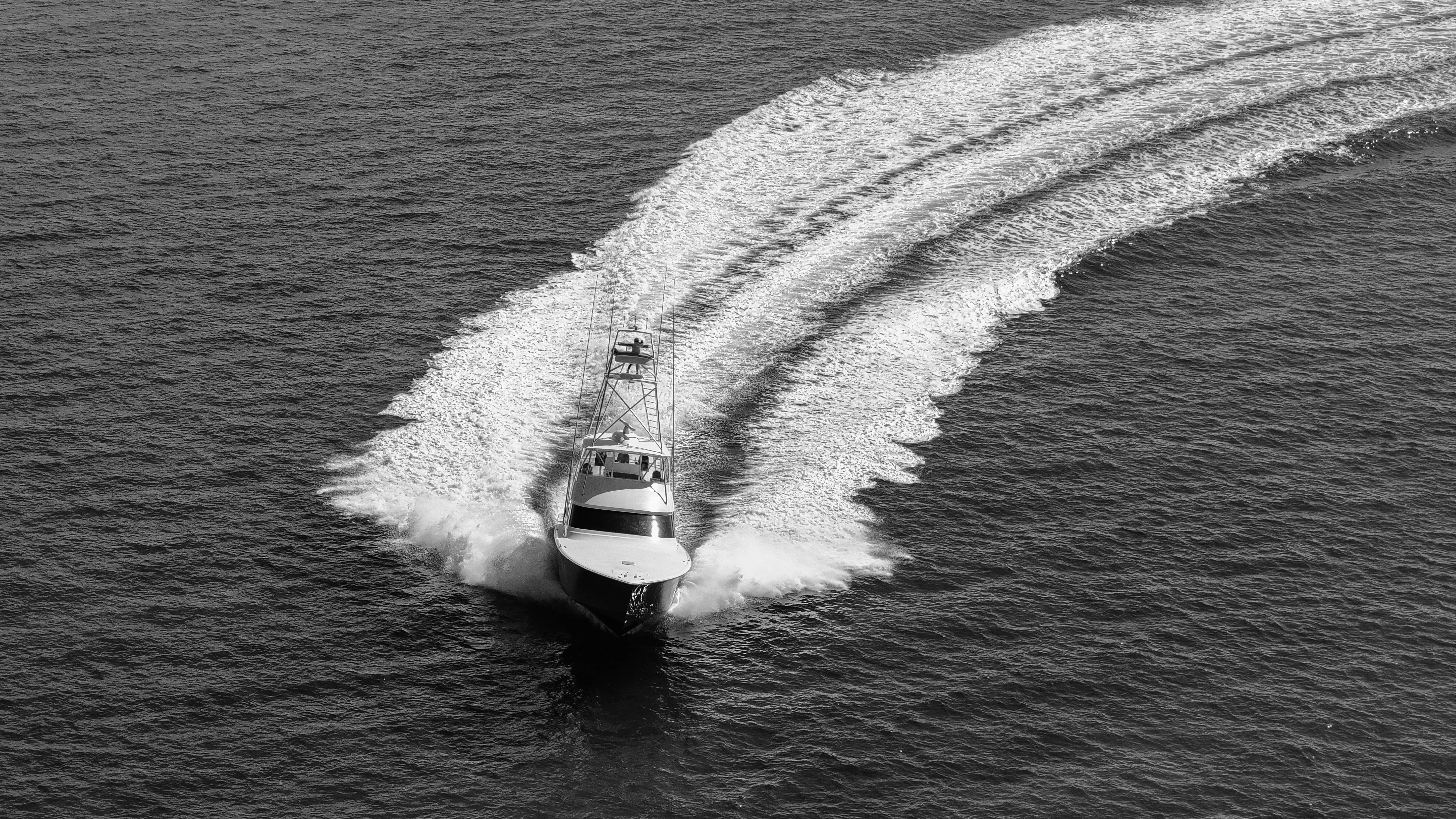 Black and white aerial view of a motorboat making a curved wake as it moves through calm ocean water.