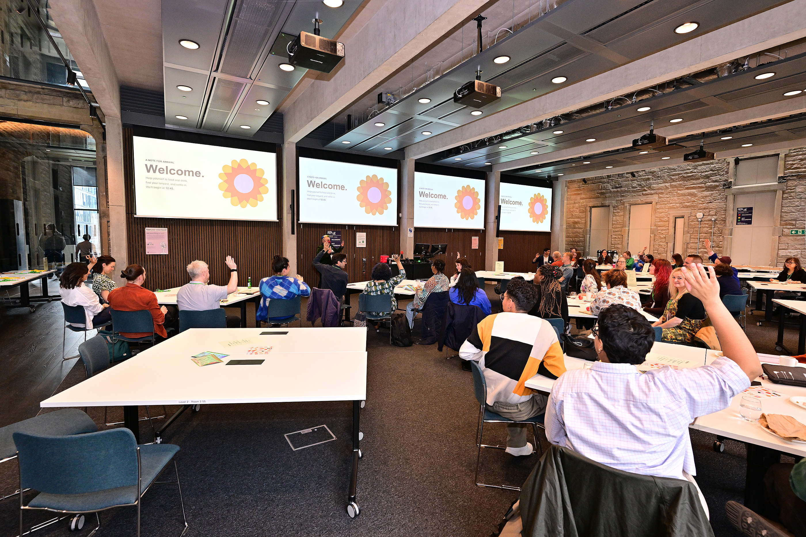 A room full of people with hands raised looking at screens with a Welcome message on it