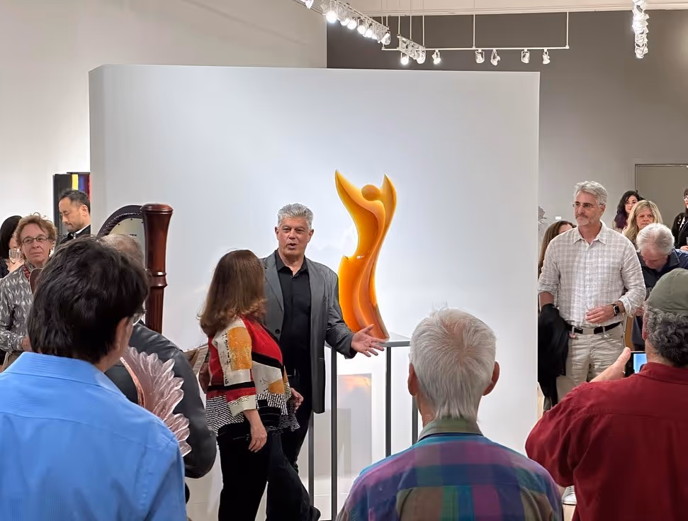 Crowd at gallery opening around orange sculpture on pedestal
