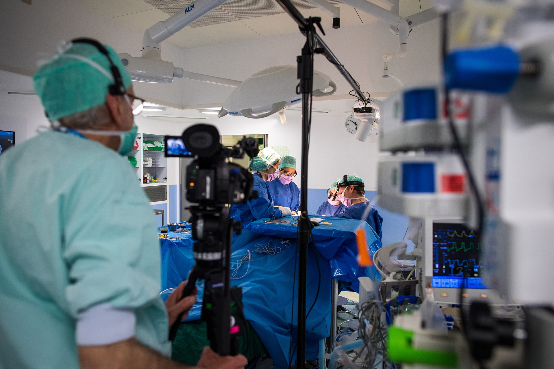 Chirurgiens en salle d'opération en tenue bleue stérile opérant un patient pendant qu'un cameraman enregistre la procédure.