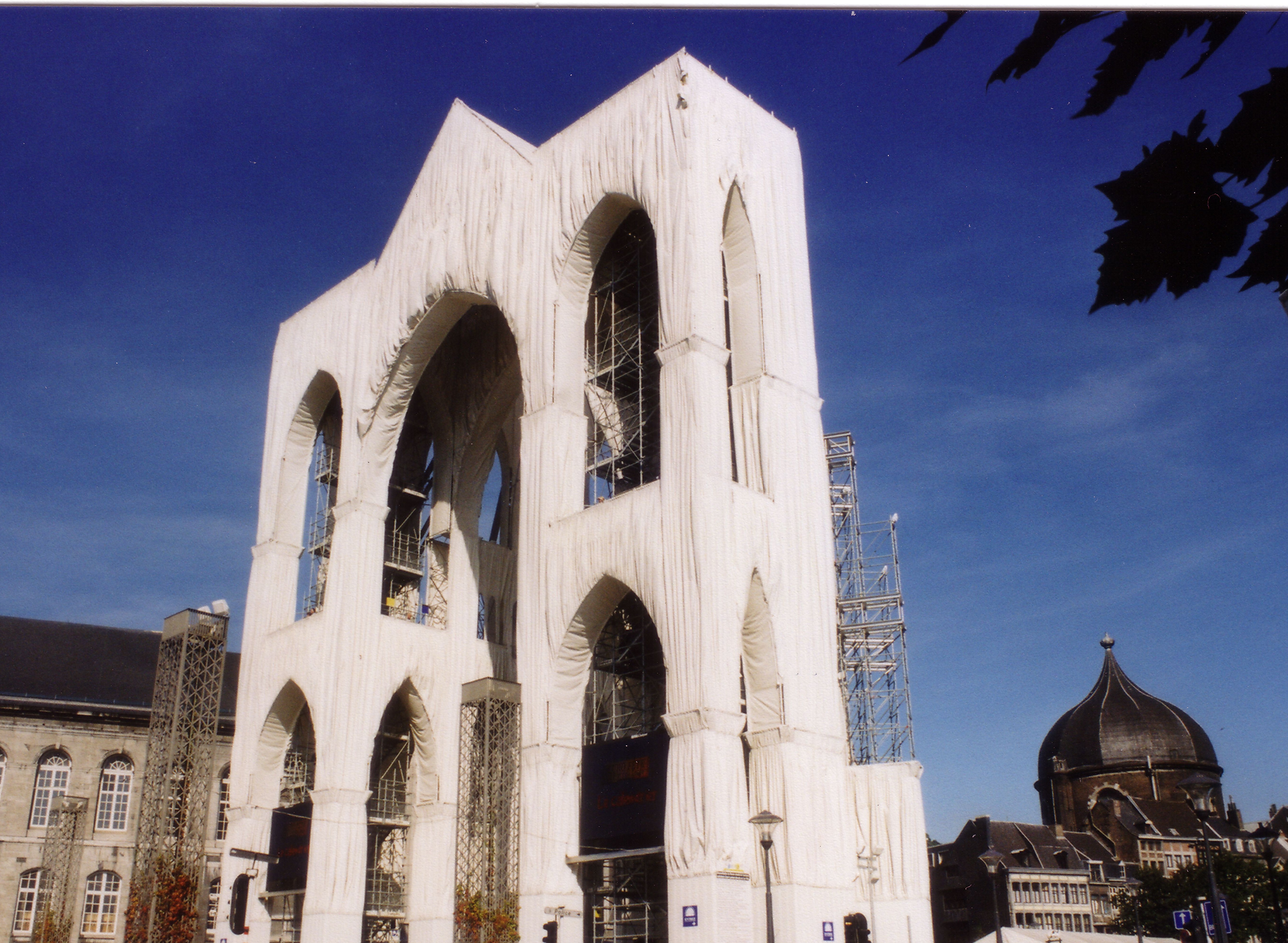 Monument architectural aux grandes arches gothiques recouvertes d'un tissu blanc lors d'une installation d'art, avec un ciel bleu en arrière-plan.