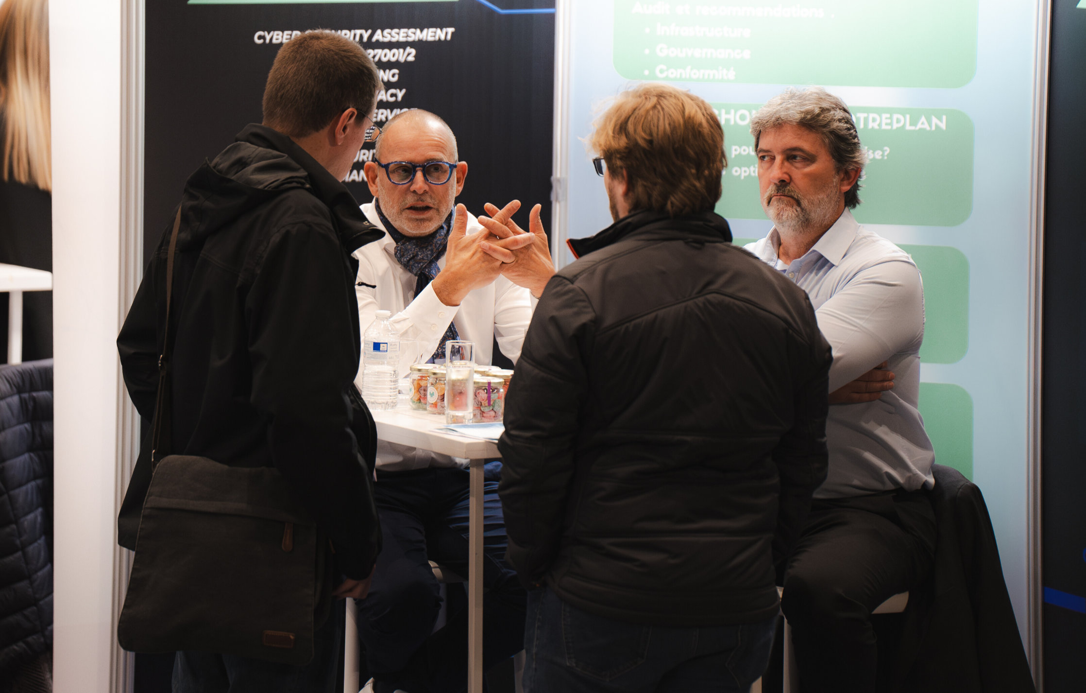 Quatre hommes discutent autour d'une table lors d'un événement professionnel axé sur la cybersécurité.