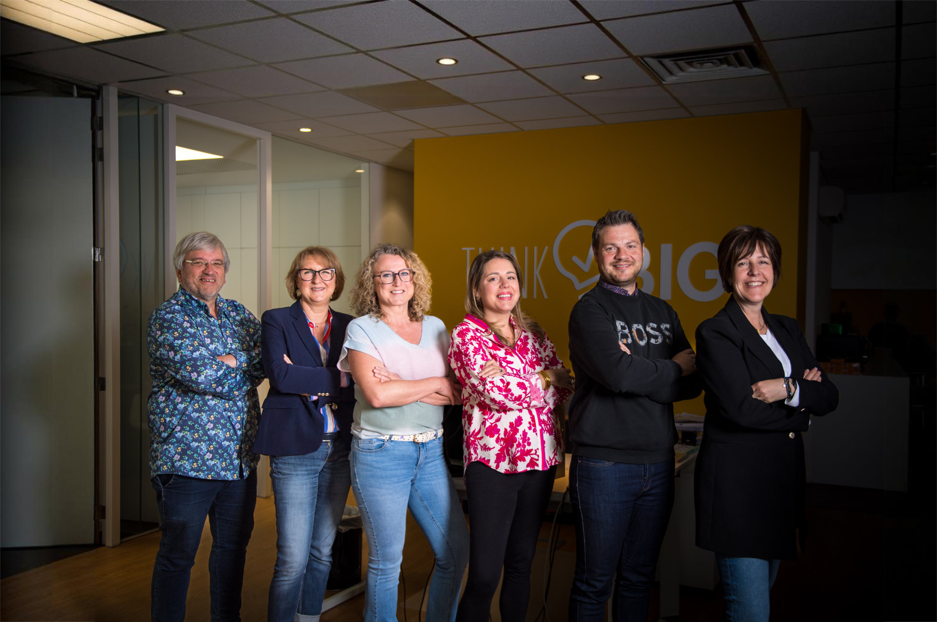L'équipe Enjeu debout en ligne, bras croisés, souriants, dans leur bureaux