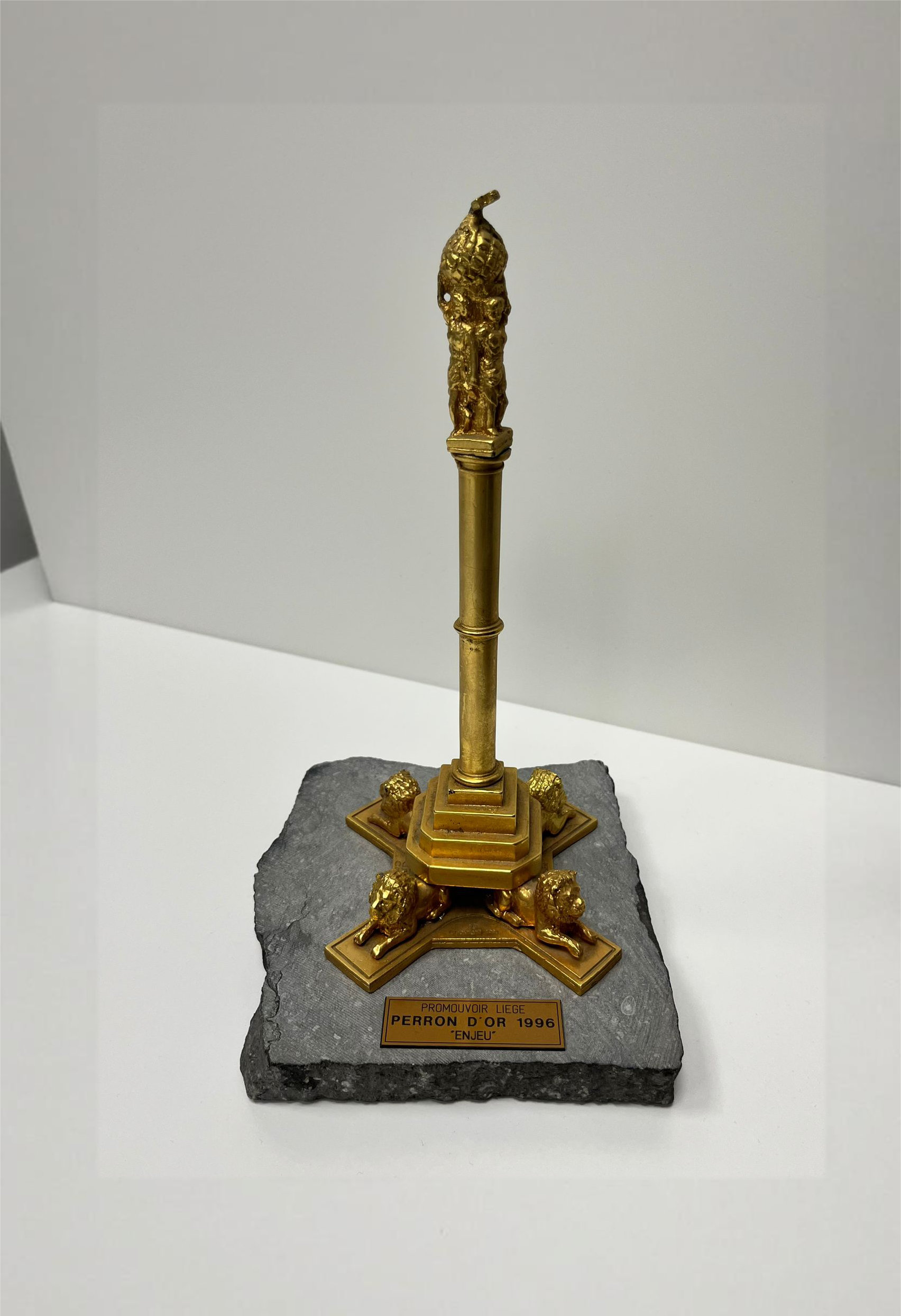 Un trophée doré sur une base en pierre avec une colonne centrale et quatre lions dorés aux coins, portant une plaque indiquant Perron d'Or 1996.