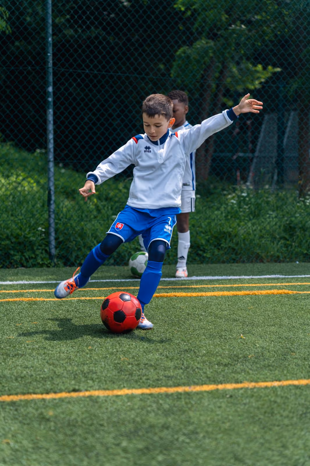 photo de Samuel un enfant de l'académie pmpk entrain d'effectuer un geste technique, il a un ballon rouge et un maillot blanc et bleu