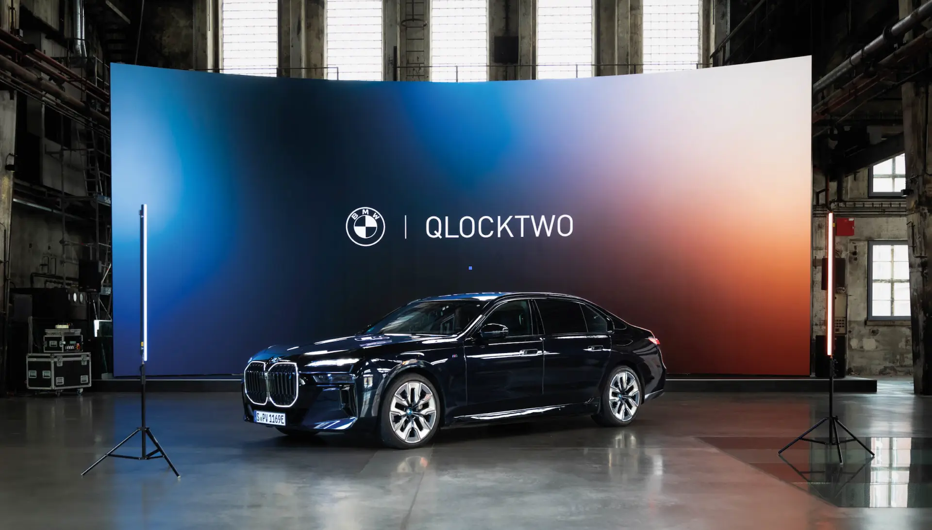 Ein Fahrzeug von BMW vor einer Leinwand mit dem Kooperationslogo von Qlocktwo und BMW
