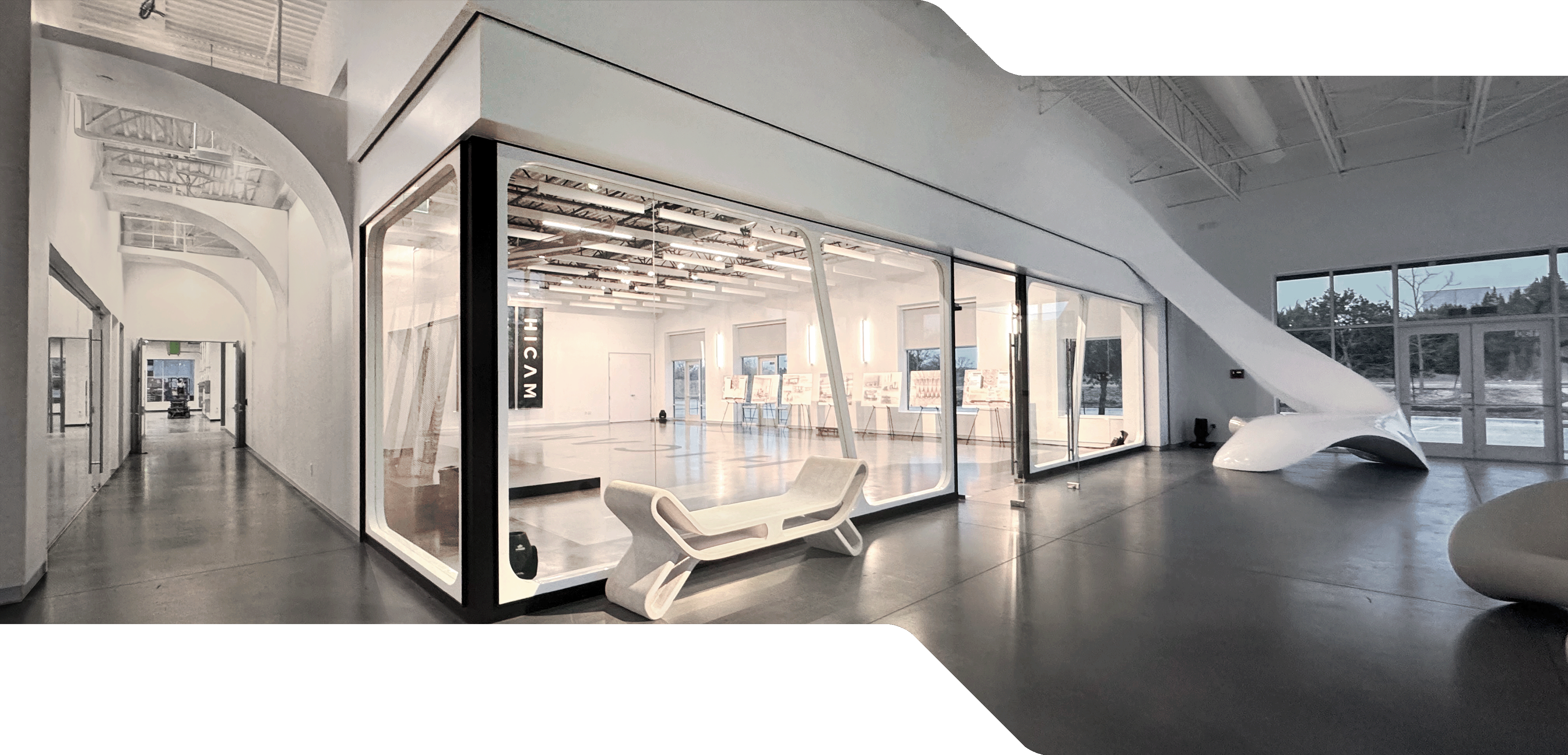 HICAM’s modern, spacious lobby with high ceilings, polished concrete floors, and sleek white architectural features. A large glass-walled event space room is centrally positioned, surrounded by sculptural furniture and natural light from large windows.