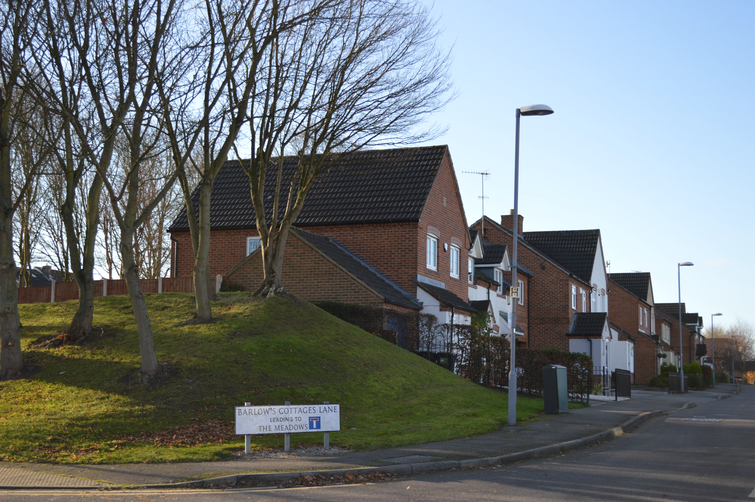 Row of brick and white cottages along a street with a sign reading Barlow's Cottages Lane leading to The Meadows.