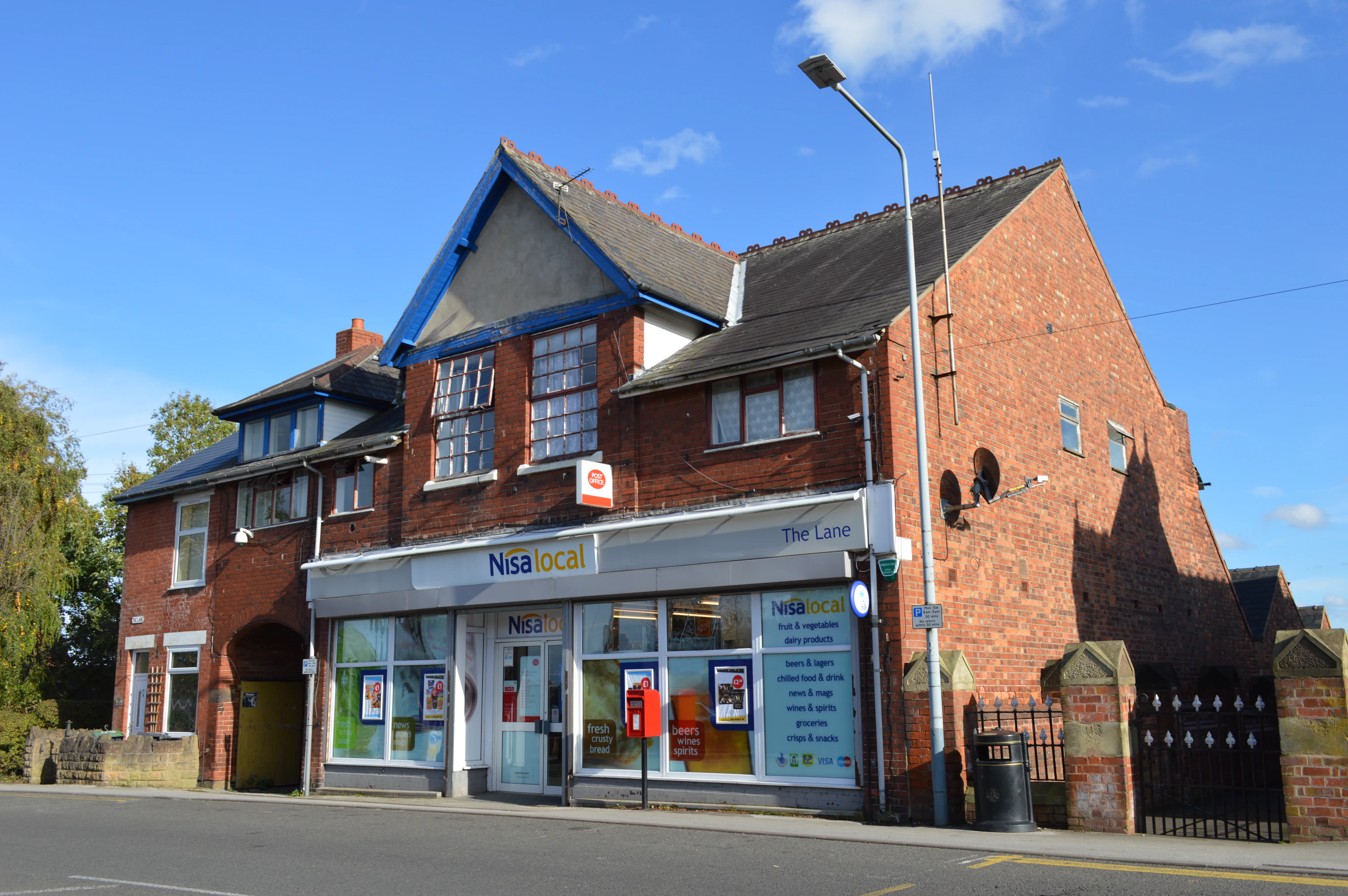 Nisa Local convenience store in a red brick building on a sunny day with blue sky.