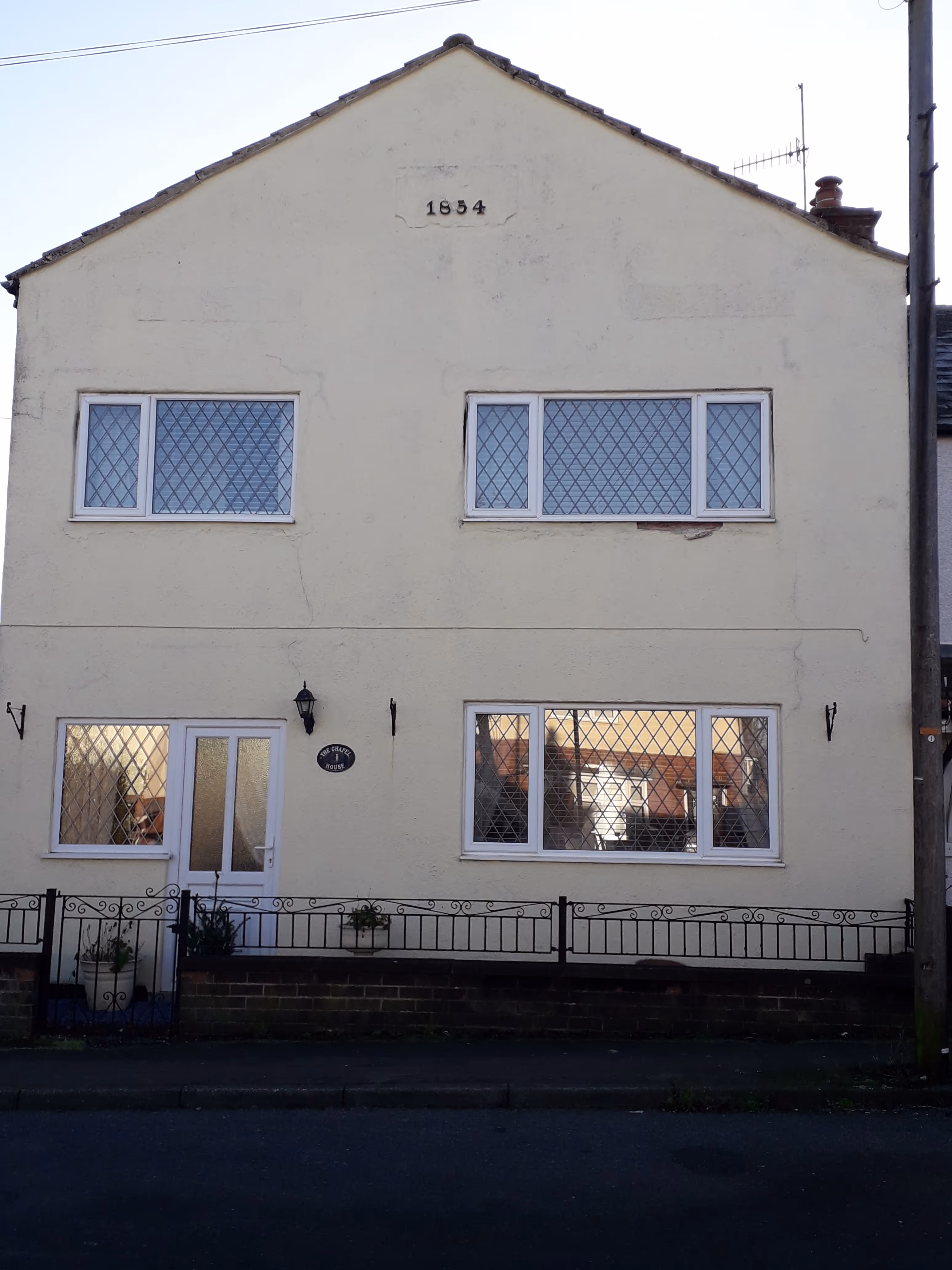 Two-story pale yellow building with diamond-patterned windows and the year 1854 inscribed near the roof.