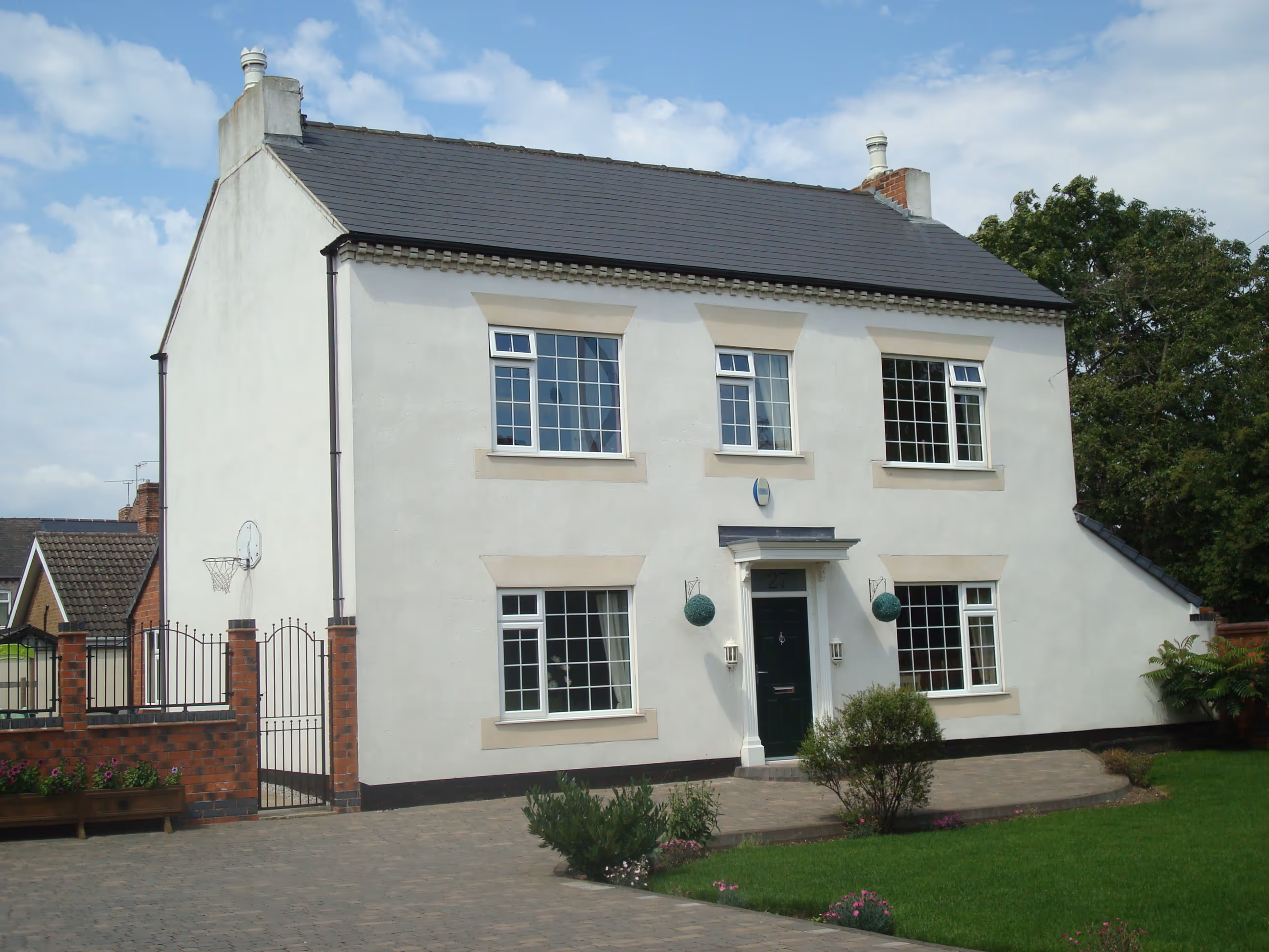 Two-story white house with black door, multiple windows, brick fence and a gate.