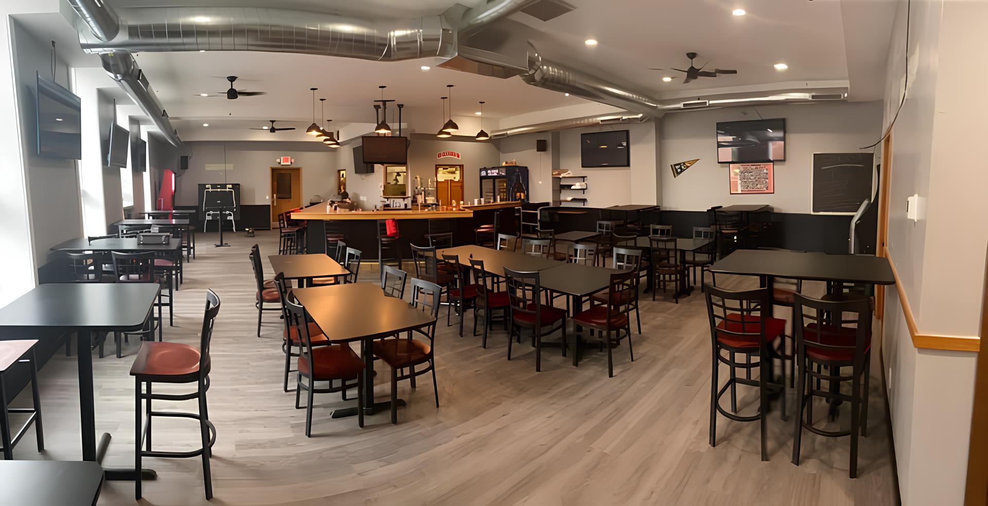 Modern bar with sleek tables and chairs arranged in rows, a central wooden bar counter, ceiling fans, and ambient lighting, conveying a cozy vibe.