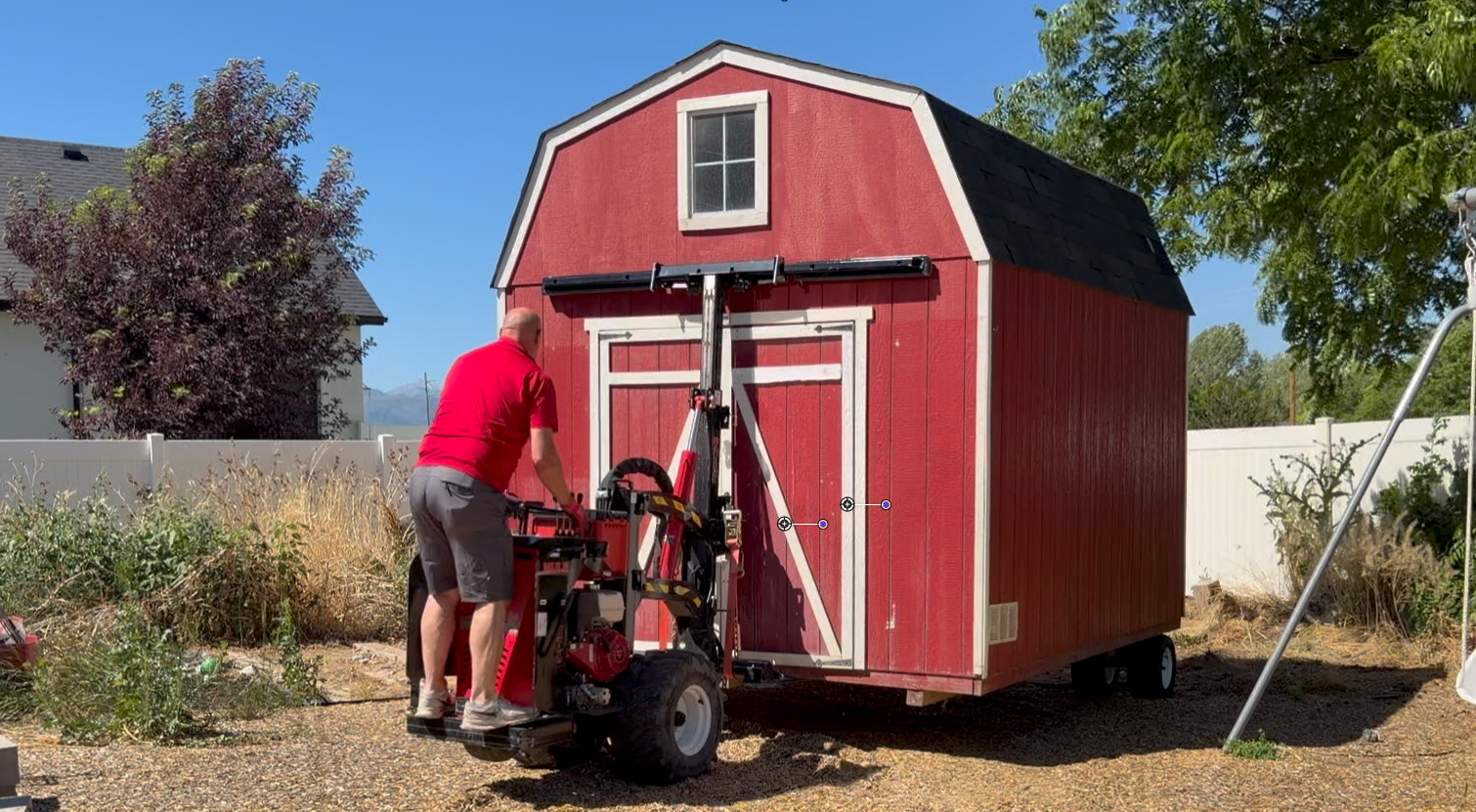 Shed moving equipment being used to reposition a red storage shed in a backyard