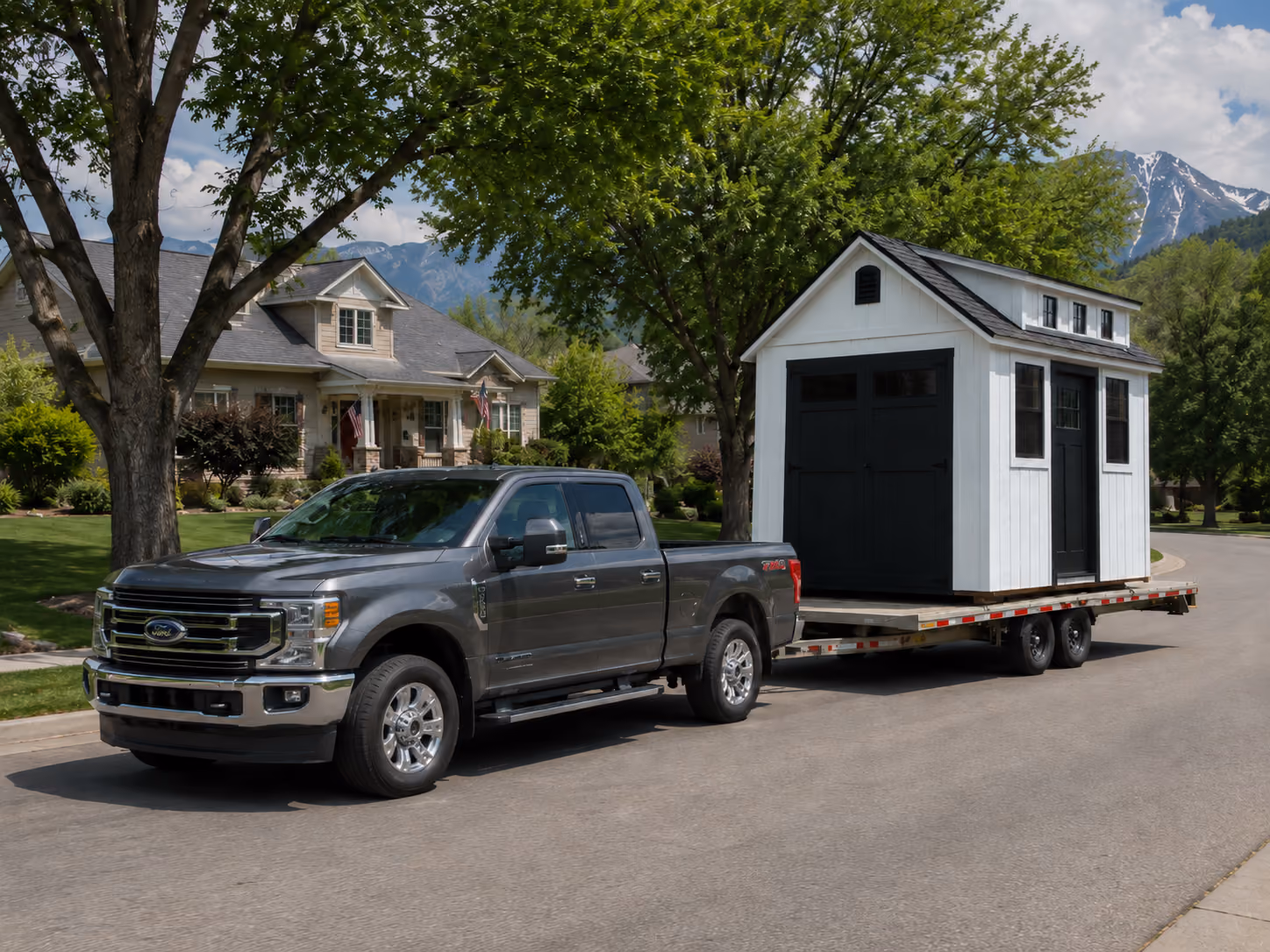 Truck hauling a storage shed on a trailer through a Utah neighborhood with large trees and mountains in the background