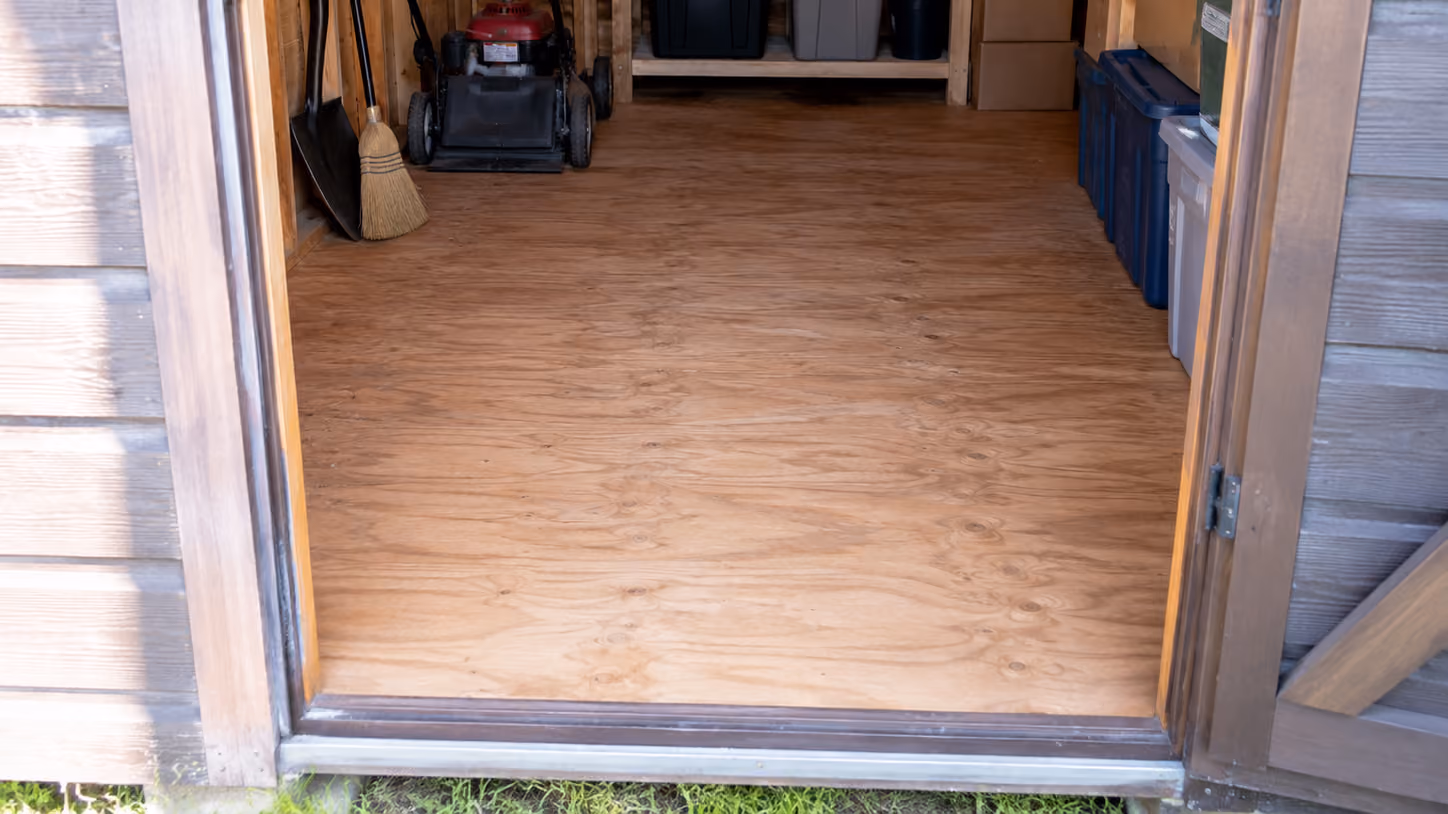 Interior view of a storage shed showing the wood floor through the open doorway