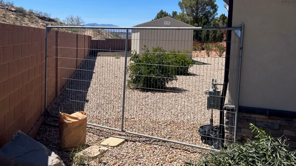 Backyard shed access path with a wide metal gate, gravel yard, and storage shed in the background.